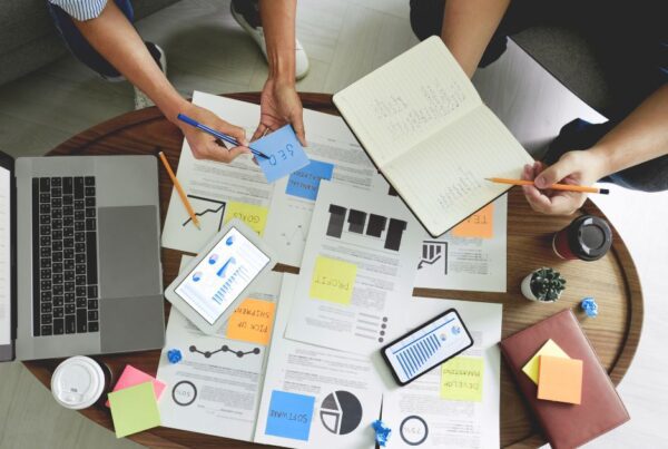 Grupo de social managers diseñando estrategias de mercadeo digital en una mesa con papeles y una computadora.