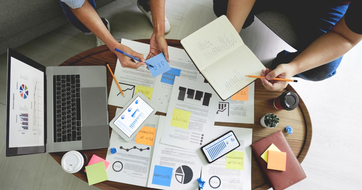 Grupo de social managers diseñando estrategias de mercadeo digital en una mesa con papeles y una computadora.